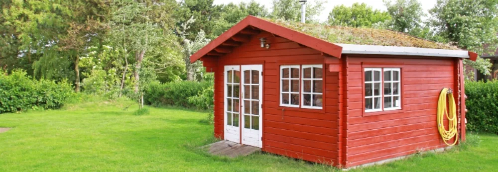 Rotes Gartenhaus mit begrünten Dach